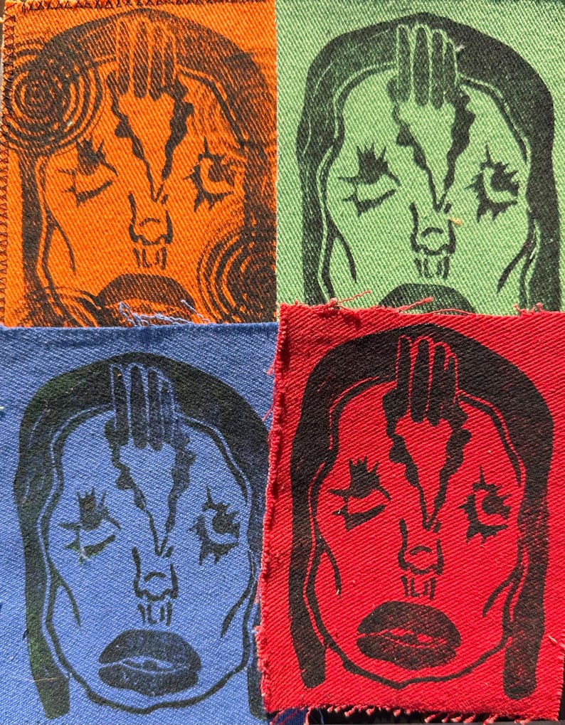 May include: Four fabric squares, each featuring a black linocut print of a stylized face with a hand above the head. The squares are in orange, green, blue, and red. The image has a handmade, artistic aesthetic.