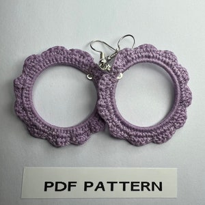 K&ouml;nnte beinhalten: Ein Paar geh&auml;kelte, lavendelfarbene Creolen mit silbernen Haken. PDF PATTERN steht auf einem wei&szlig;en Etikett unter den Ohrringen.