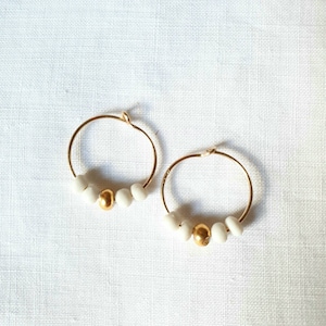 May include: A pair of gold hoop earrings with white beads and a gold bead in the centre of each hoop.