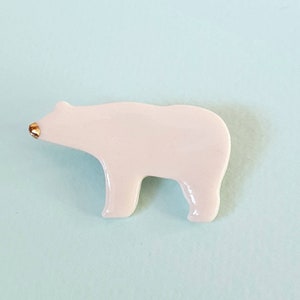 Può includere: Statuetta di orso polare rosa chiaro con naso color oro. L'orso è in piedi sulle quattro zampe. La statuetta è realizzata in materiale lucido ed è posta su uno sfondo azzurro.