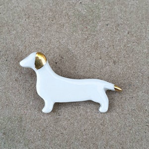 May include: White ceramic dachshund figurine with a gold-painted head and tail.