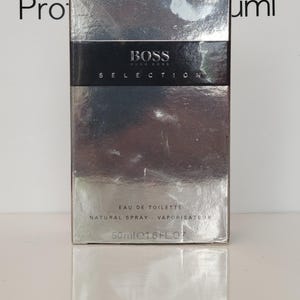 Könnte beinhalten: Eine rechteckige, silberfarbene Schachtel mit BOSS Selection Eau de Toilette. Der Marken- und Produktname ist in schwarzer Schrift dargestellt. Der Boden der Schachtel zeigt ein Volumen von 50 ml (1,6 fl oz).