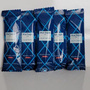 Könnte beinhalten: Fünf kleine, dunkelblaue Parfümproben. Jede Probe hat ein weißes Etikett mit dem Text "Blue Sugar man Eau de Toilette" und dem Markennamen "AQUOLINA". Jede Probe enthält 1,8 ml oder 0,06 fl. oz.