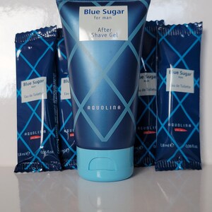 May include: A blue tube of "Blue Sugar for man After Shave Gel" with a light blue cap, surrounded by four small packets of "Blue Sugar man Eau de Toilette". The products have a geometric design and the brand name "AQUOLINA".
