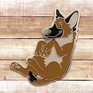 May include: A gold-colored enamel pin of a brown and black German Shepherd puppy, curled up with its paws tucked under its chin. The puppy is looking to the right of the image.