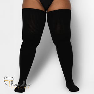 May include: Black, ribbed thigh-high socks. The socks cover the legs from the feet to the upper thighs. The brand name "Thunda Thighs" is visible in the lower left corner. The background is plain white.