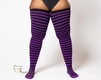 May include: Thigh-high socks featuring a horizontal striped pattern in alternating black and purple colors. The socks have a ribbed texture and extend from the feet up to the upper thigh area. A logo with the text Thunda Thighs is visible.