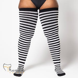 May include: Black and white striped thigh-high socks. The socks feature alternating thick stripes of black and white, extending from the toes to the upper thigh. The socks are made of a soft, stretchy material.