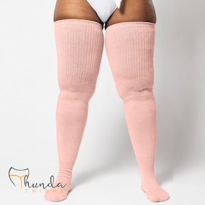 May include: Pale pink thigh-high socks with a ribbed knit texture. The socks extend from the feet to the upper thighs. The brand logo "Thunda Thighs" is visible in the lower left corner.