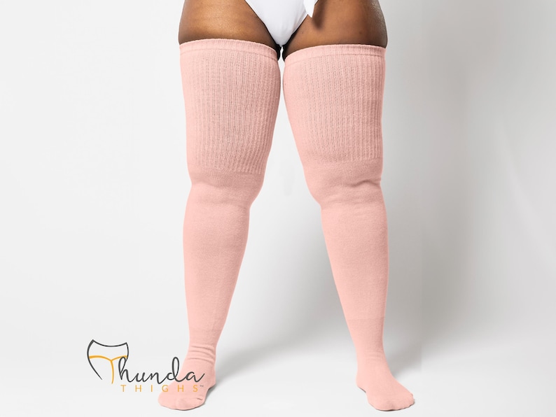 May include: Pale pink thigh-high socks with a ribbed knit texture. The socks extend from the feet to the upper thighs. The brand logo "Thunda Thighs" is visible in the lower left corner.