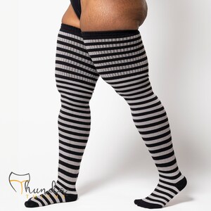 May include: Over-the-knee socks with alternating black and gray horizontal stripes. The socks have a black cuff at the top and black toes and heels. The socks are made of a soft, stretchy material.