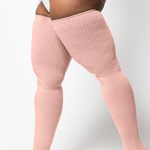 May include: A pair of pale pink, ribbed-knit thigh-high socks. The socks are made of a soft material and extend from the feet to the upper thighs. The socks are a solid color and have a simple, classic design.