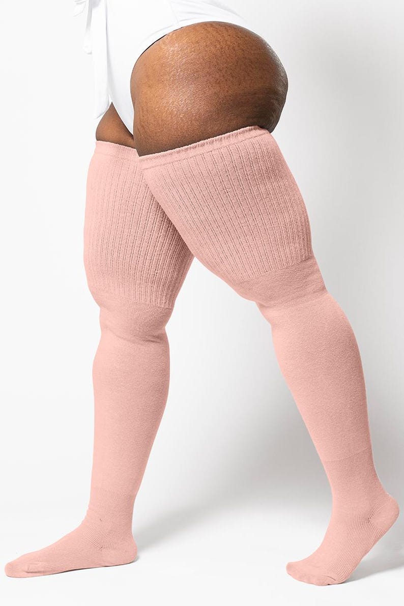 May include: A pair of pale pink, ribbed-knit thigh-high socks. The socks are made of a soft material and extend from the feet to the upper thighs. The socks are a solid color and have a simple, classic design.