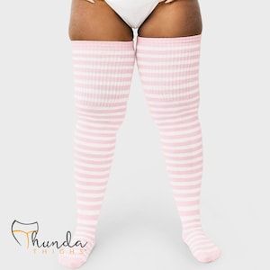 Peut inclure: Chaussettes hautes à rayures roses et blanches. Les chaussettes sont côtelées et présentent des rayures horizontales. La marque "Thunda Thighs" est visible dans le coin inférieur gauche.