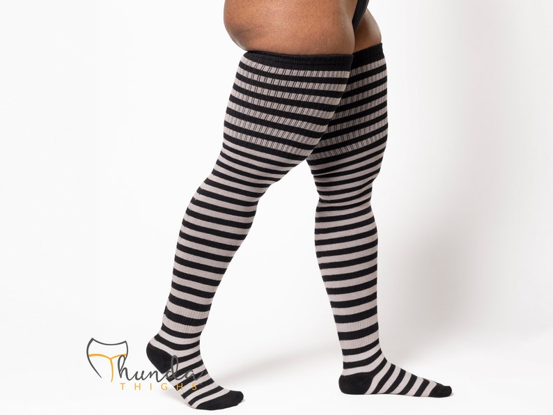 May include: Over-the-knee striped socks in black and gray. The socks feature a horizontal stripe pattern and are designed to reach the upper thigh. The socks have a black cuff and foot, with the brand logo visible.
