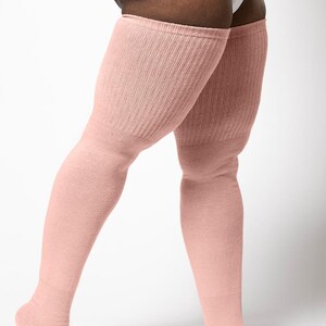 May include: Pale pink over-the-knee socks. The socks are made of a soft, ribbed knit material. The socks extend from the foot to the mid-thigh. The socks are a solid color and have a simple, classic design. The socks are a light, neutral color.