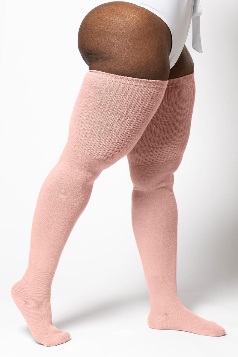 May include: Pale pink over-the-knee socks. The socks are made of a soft, ribbed knit material. The socks extend from the foot to the mid-thigh. The socks are a solid color and have a simple, classic design. The socks are a light, neutral color.