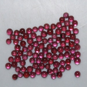 May include: A large group of round, red gemstones. The gemstones are smooth and shiny, and they are all about the same size.