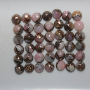 May include: A collection of 36 round, pink opal cabochons with copper inclusions. The cabochons are approximately 6mm in diameter and have a smooth, polished finish.