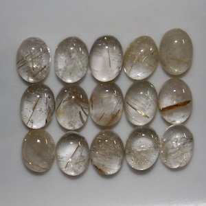 May include: Fifteen oval-shaped, clear quartz cabochons with gold rutile inclusions. The cabochons are approximately 1 inch in length.
