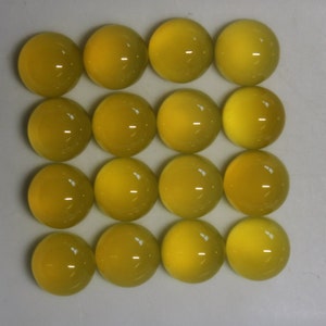 May include: Sixteen round, yellow cabochon gemstones arranged in four rows of four. Each polished stone has a smooth, domed surface and a bright, translucent appearance. The gemstones are a consistent size and shape, with a slight variation in color.