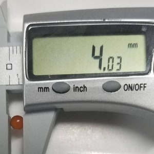 Puede incluir: Primer plano de un calibre digital que mide una peque&ntilde;a cuenta redonda de color naranja. El calibre muestra 4,03 mm.