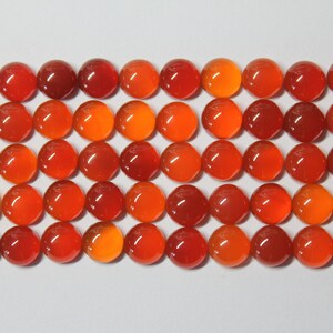 Puede incluir: Una colecci&oacute;n de 40 cabujones redondos de cornalina naranja. Los cabujones est&aacute;n dispuestos en una cuadr&iacute;cula sobre una superficie blanca.
