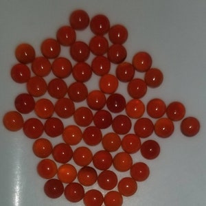 Puede incluir: Una colecci&oacute;n de aproximadamente 50 piedras redondas de cornalina naranja. Las piedras son lisas y pulidas, y est&aacute;n dispuestas en un patr&oacute;n suelto y org&aacute;nico.