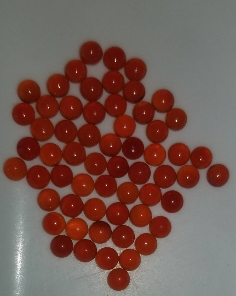 Puede incluir: Una colecci&oacute;n de aproximadamente 50 piedras redondas de cornalina naranja. Las piedras son lisas y pulidas, y est&aacute;n dispuestas en un patr&oacute;n suelto y org&aacute;nico.