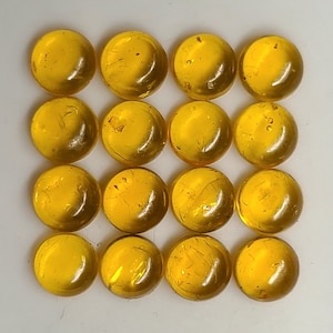 May include: A set of 16 round, amber-coloured glass tiles. The tiles are smooth and shiny, with a slight variation in colour.