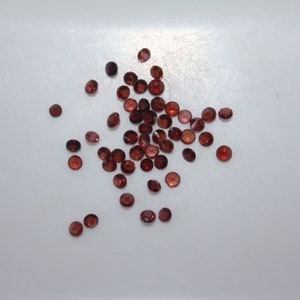 May include: A scattering of small, round, red gemstones on a white surface.