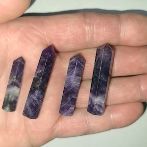 May include: Four amethyst crystal wands of varying sizes, with a purple and white color pattern, are displayed on a hand.