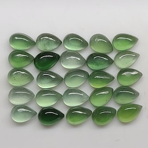 May include: Twenty-five pear-shaped green gemstones, some with a lighter shade than others, arranged in rows on a white surface.