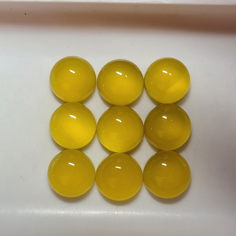 May include: Nine bright yellow, spherical gemstones are arranged in a grid pattern. The polished stones have a glossy finish, reflecting light. The gems are set against a white background, highlighting their vibrant color and shape.