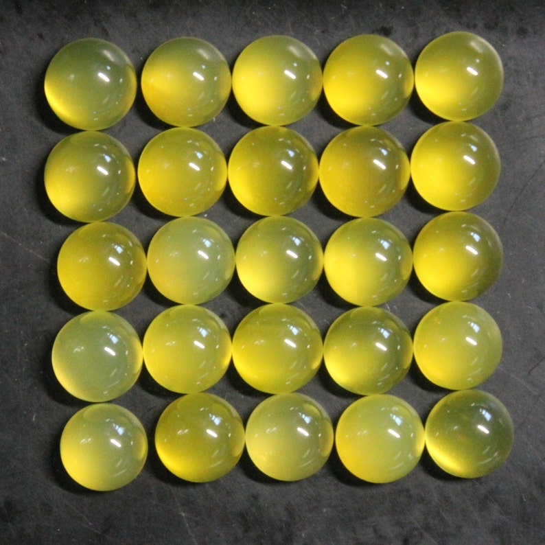 May include: Twenty-five translucent, round, yellow-green cabochons arranged in a grid pattern. Each cabochon has a smooth, polished surface and a slight internal glow. The gems are evenly sized and appear to be made of glass or a similar material.