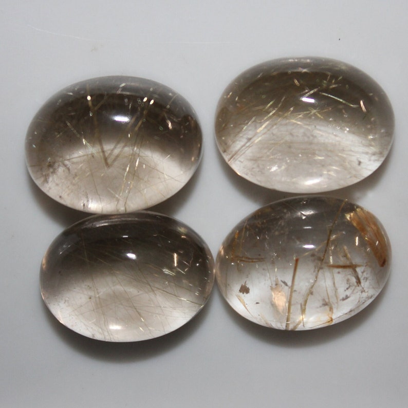 May include: Four oval-shaped, translucent, light brown gemstones with gold inclusions. The gemstones are smooth and polished.