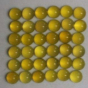 May include: A grid of thirty-six yellow cabochon gemstones. Each gemstone is round with a polished, domed surface. The color varies slightly from pale to a deeper yellow. The gemstones are arranged in a square pattern.