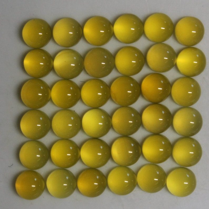 May include: A grid of thirty-six yellow cabochon gemstones. Each gemstone is round with a polished, domed surface. The color varies slightly from pale to a deeper yellow. The gemstones are arranged in a square pattern.