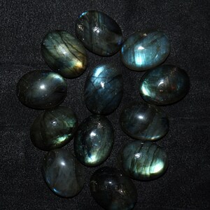 May include: A collection of 12 oval-shaped labradorite gemstones. The stones are a deep green with iridescent blue and gold flashes.