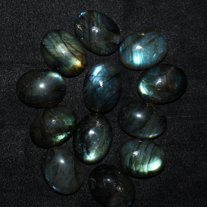 May include: A collection of 12 oval-shaped labradorite gemstones. The stones are a deep green with iridescent blue and gold flashes.