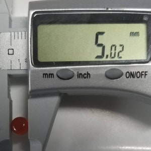 Puede incluir: Una piedra preciosa roja que se mide con un calibre digital. El calibre muestra 5,02 mm.