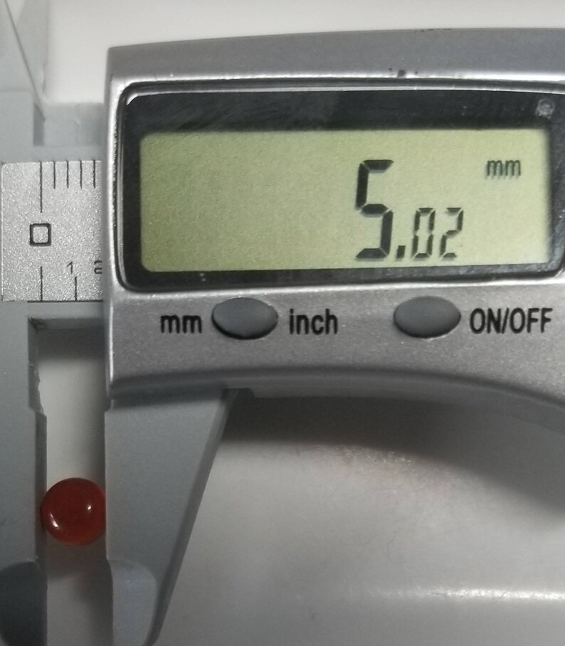 Puede incluir: Una piedra preciosa roja que se mide con un calibre digital. El calibre muestra 5,02 mm.