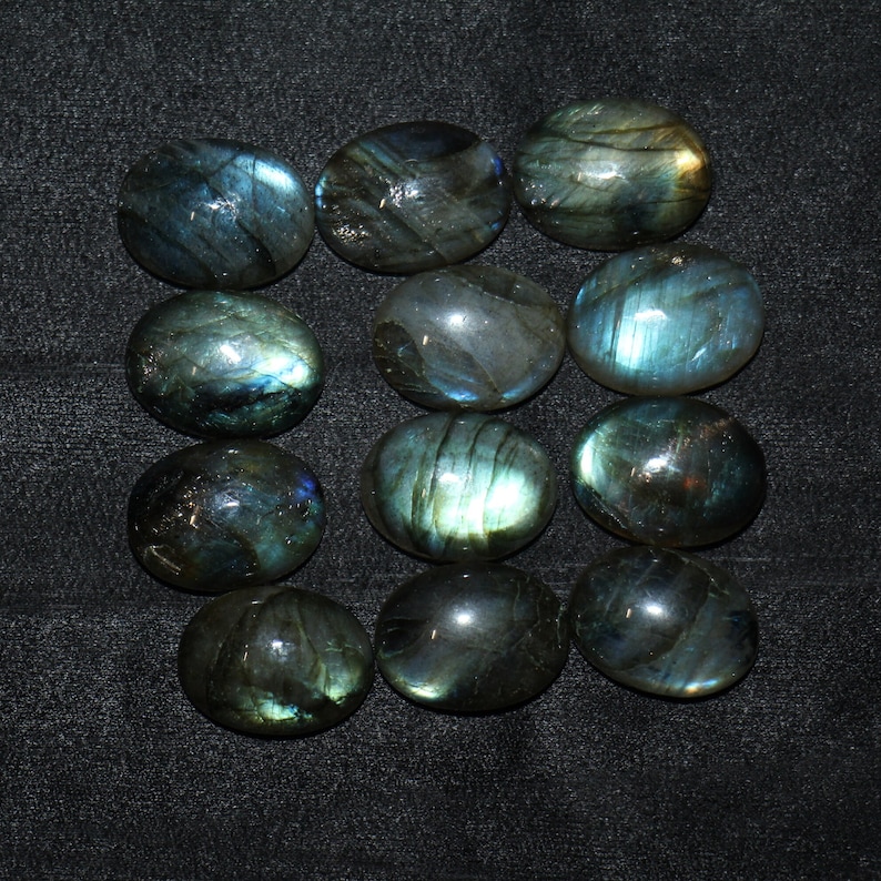 May include: Twelve oval-shaped labradorite gemstones with iridescent blue and green hues. The stones are arranged in three rows of four.