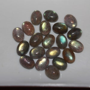 May include: A collection of oval-shaped labradorite gemstones in various shades of gray, green, and gold. The stones have a shimmering, iridescent effect.