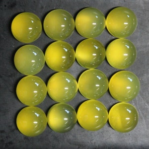 May include: Sixteen round, translucent, yellow-green gemstones are arranged in a grid pattern. Each stone has a smooth, polished surface, reflecting light. The gemstones are likely cabochons, suitable for jewelry making or other crafts.