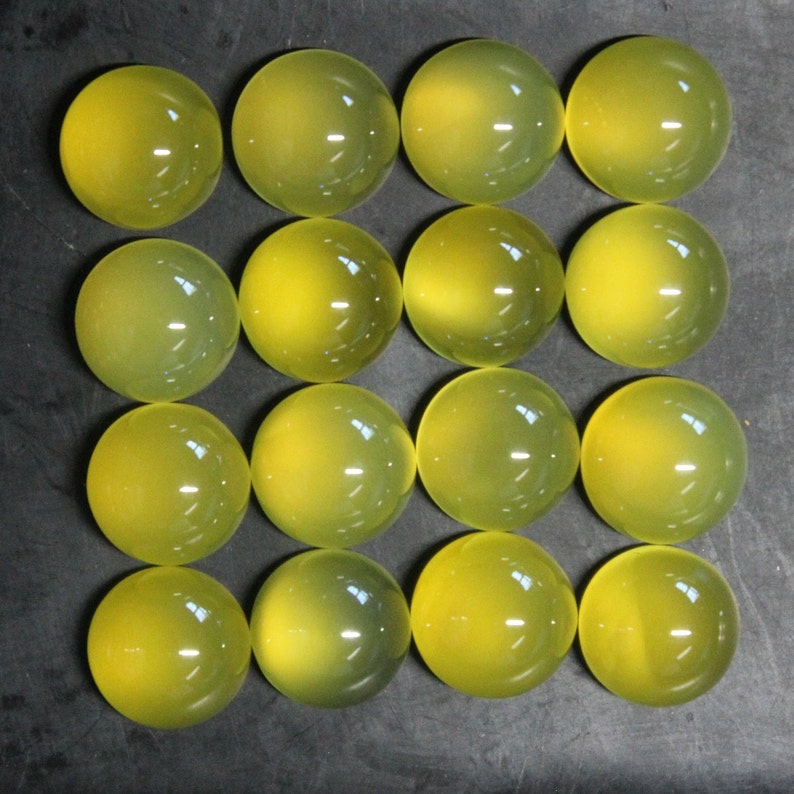 May include: Sixteen round, translucent, yellow-green gemstones are arranged in a grid pattern. Each stone has a smooth, polished surface, reflecting light. The gemstones are likely cabochons, suitable for jewelry making or other crafts.