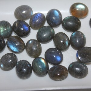May include: A collection of oval-shaped labradorite gemstones, with a variety of blue, green, and gray hues. The stones are smooth and polished, with a subtle iridescent sheen.