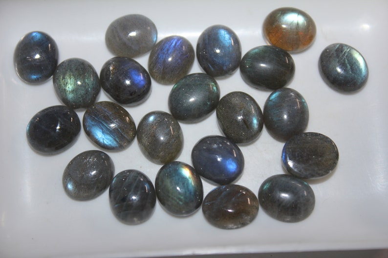 May include: A collection of oval-shaped labradorite gemstones, with a variety of blue, green, and gray hues. The stones are smooth and polished, with a subtle iridescent sheen.