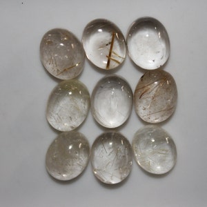 May include: Ten oval-shaped, clear quartz cabochons with gold rutile inclusions. The cabochons are smooth and polished.
