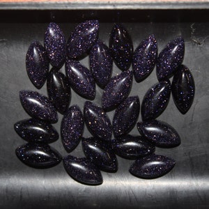 May include: A collection of 25 dark blue, oval-shaped, gemstone cabochons with a sparkly, speckled texture.